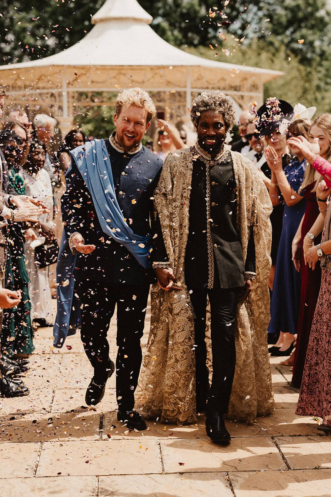 two grooms celebrating amidst confetti shower at their Cotswold wedding.