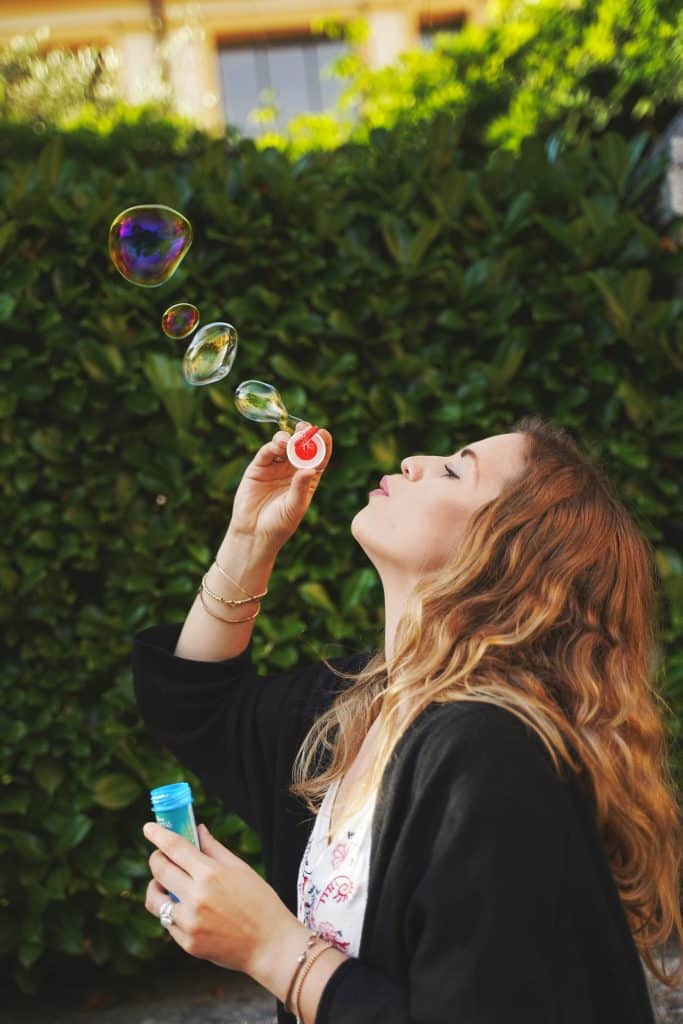 Woman blowing bubbles outdoors, smiling.